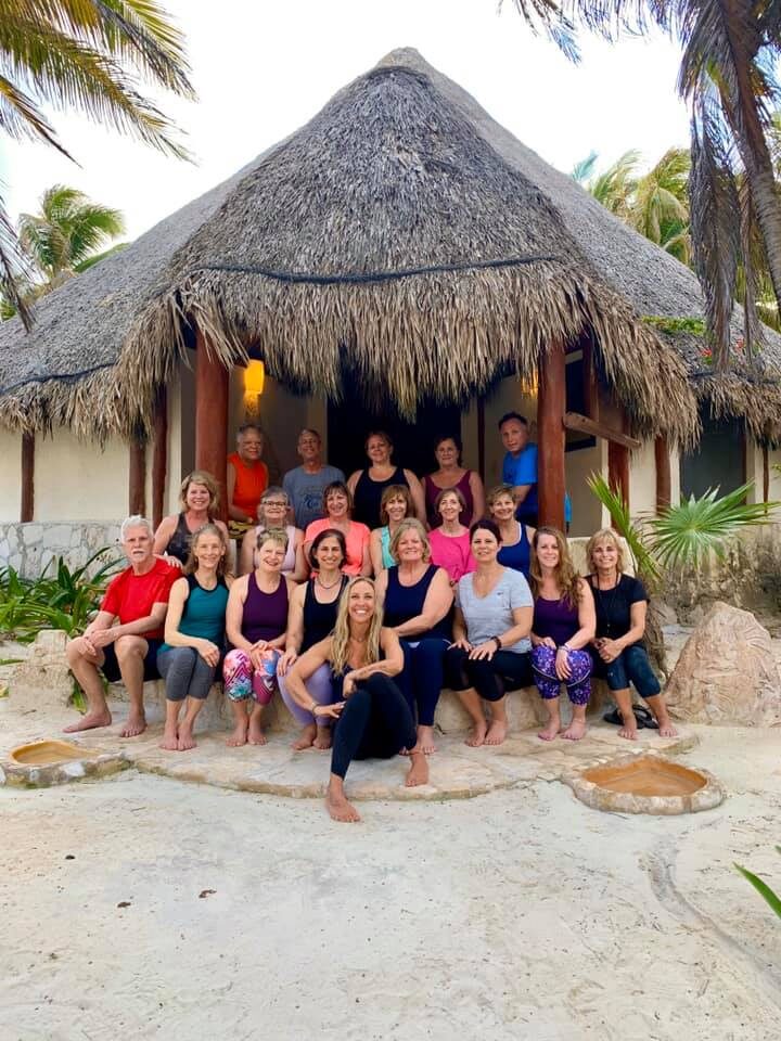 Guests smiling in front of a thatched palapa on the beach