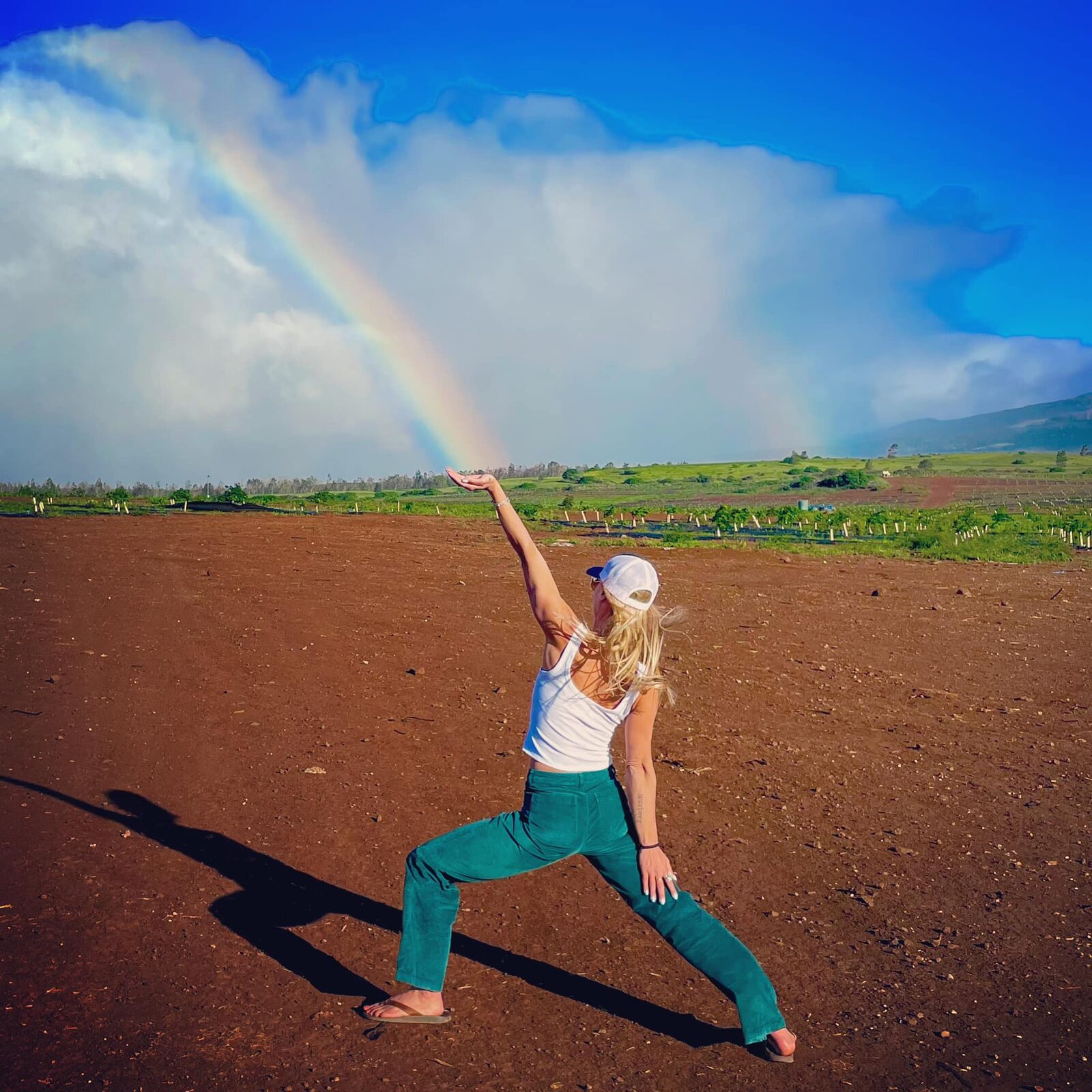 Tanya holding warrior pose beneath a rainbow on red volcanic earth